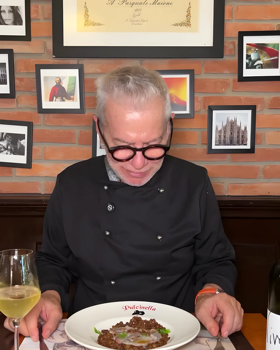 Pasquale Maione en una mesa del salón, con cuadros en la pared de ladrillo