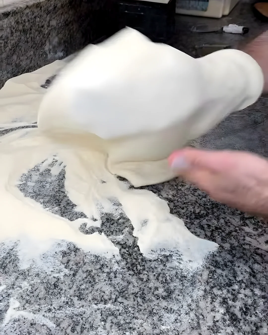 Masa de pizza estirada a mano sobre granito enharinado